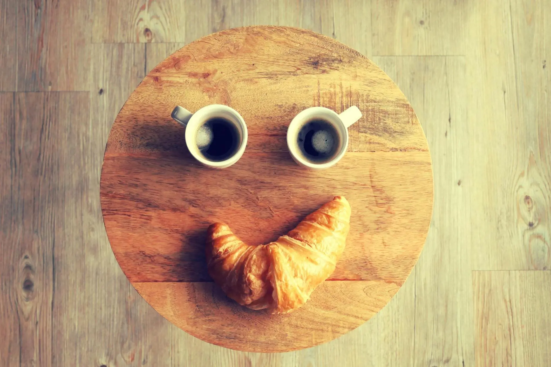 two coffees and a croissant lying on a table making a smiley face