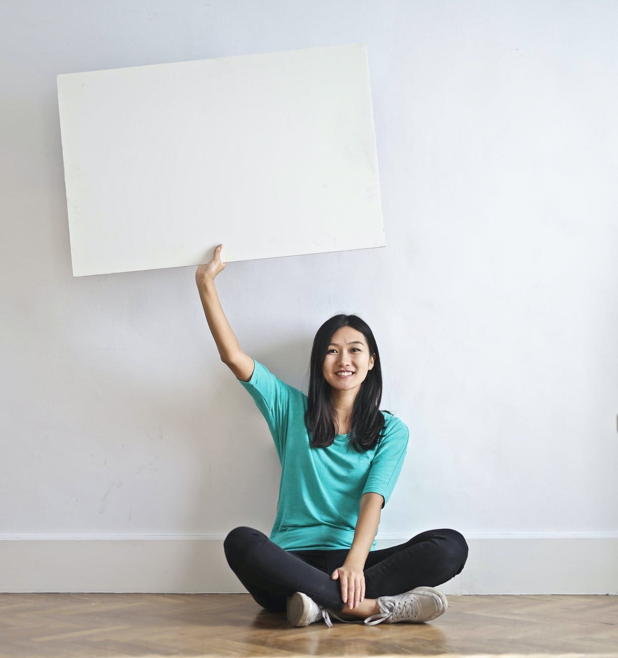 smiling ethnic woman with blank poster in empty flat looking for real estate coaching