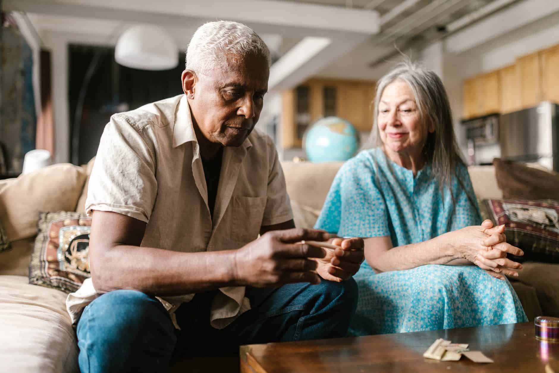 photo of an elderly man sitting on sofa while rolling a joint